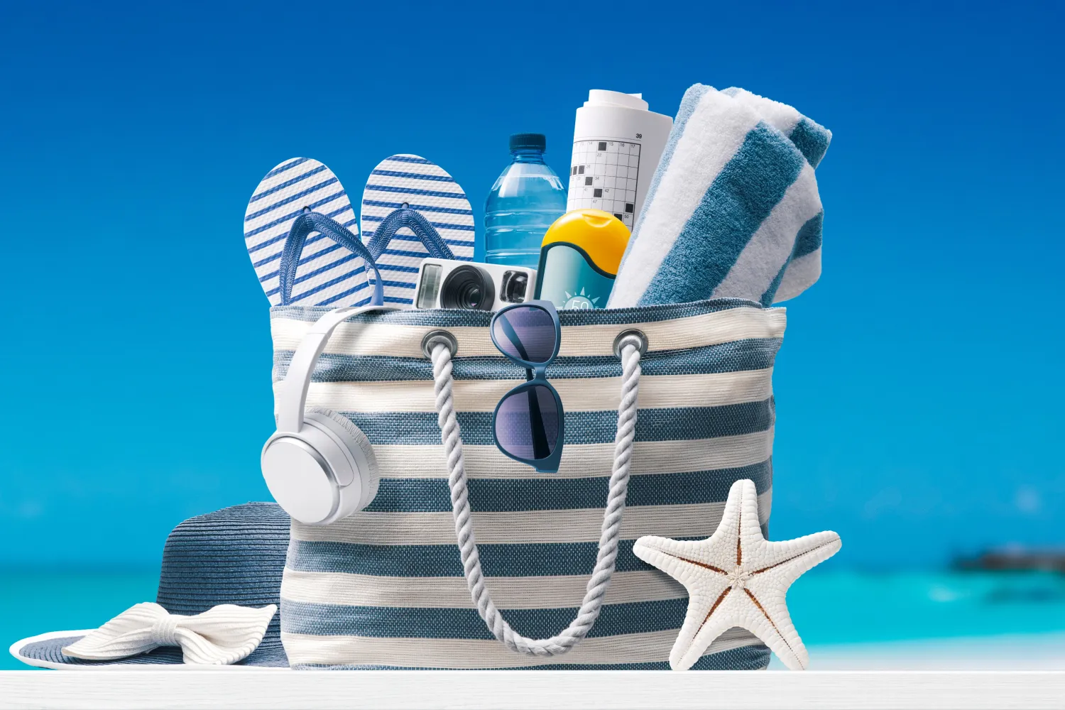 Allgemeine stilvolle Strandtasche mit Accessoires und tropischem Strand im Hintergrund.