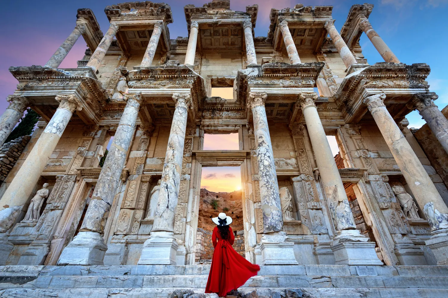 Frau in rotem Kleid, die sich die Bibliothek des Celsus in Ephesus, Türkei, ansieht